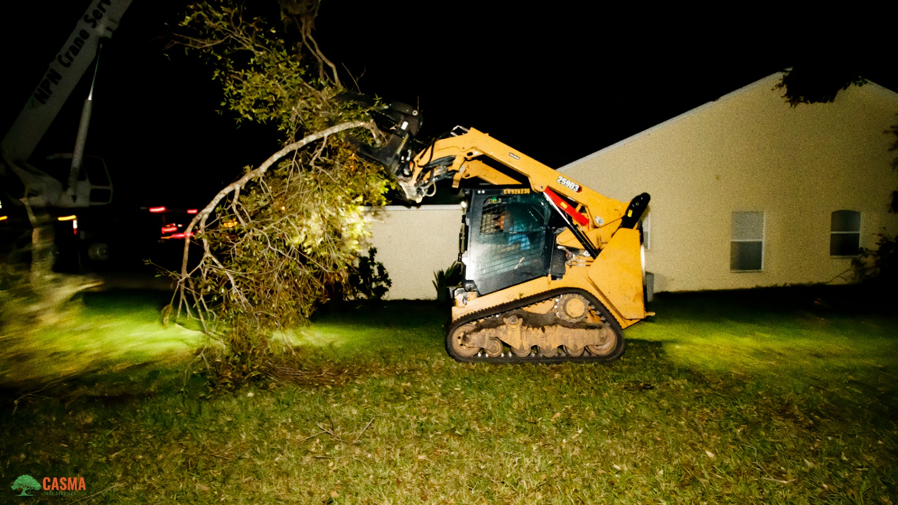 Skid steer carrying large tree limb to crane at night
