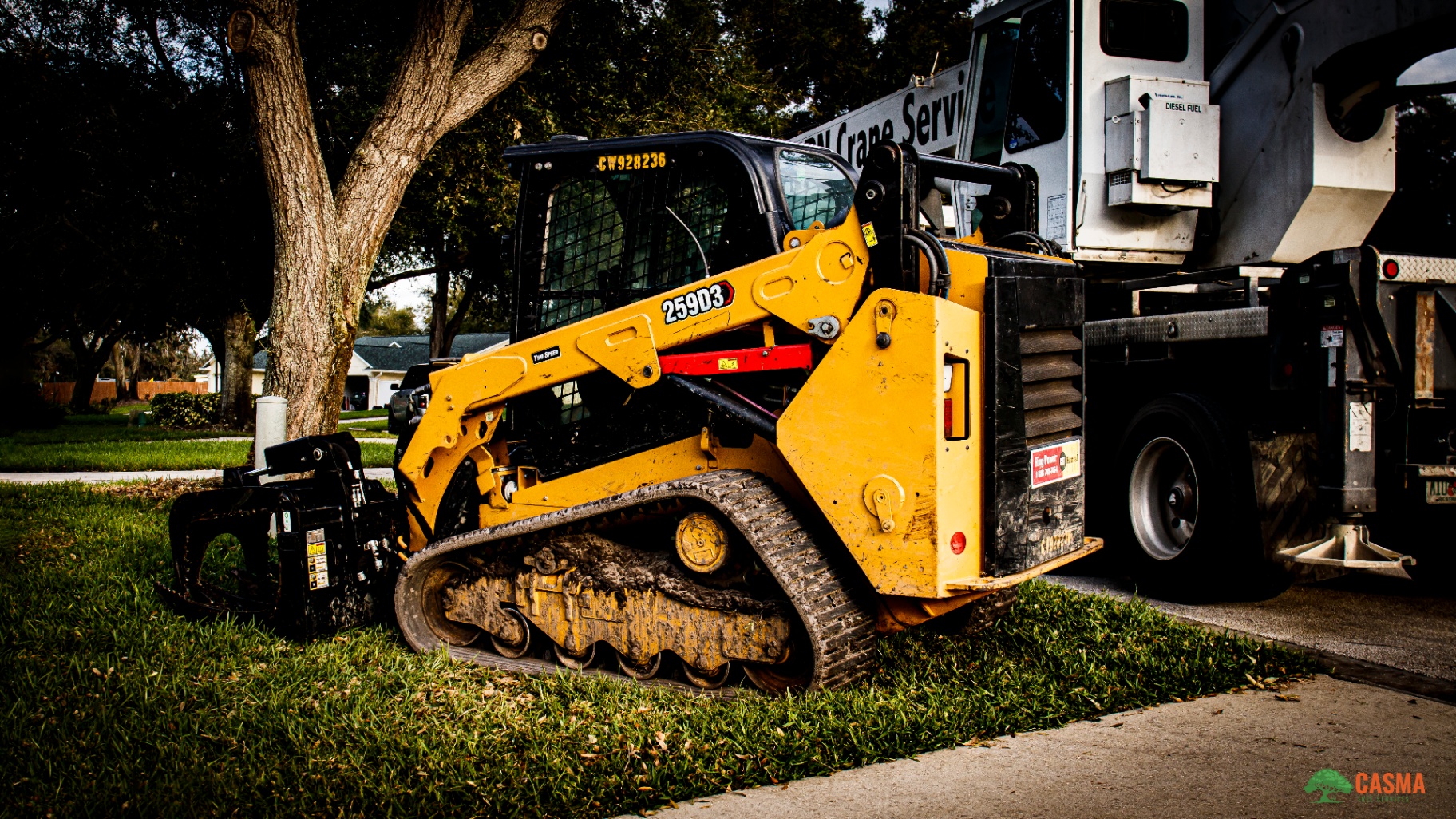 CAT 259D3 skid steer with grapple working alongside crane truck